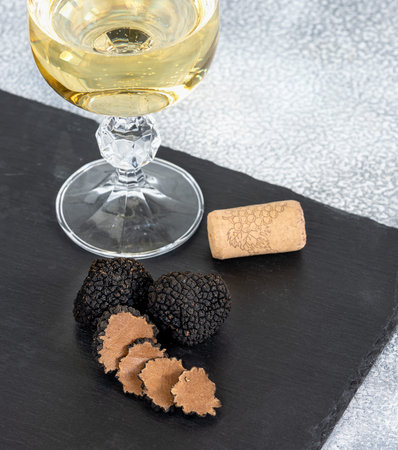 Black truffles and slices with white wine on black stone background.