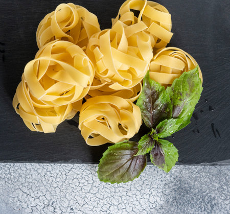 Rolled tagliatelle shape of italian pasta with basil on black stone background.