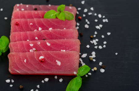 Fresh raw tuna steak with basil. On black rustic background. Copy space