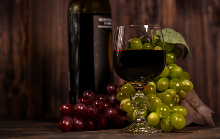 Red wine in glass with vintage bottle and with bunch of red and white grapes on wooden dark background.の写真素材