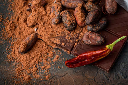 Dark chocolate, red chilli peppers, cocoa beans and powder on a dark stone background, top view, selective focus.の写真素材