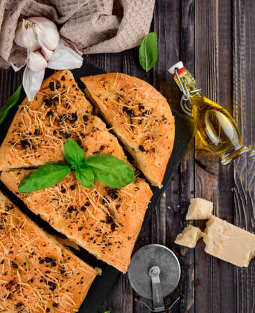 Traditional homemade Italian flat bread focaccia. Focaccia with garlic, parmesan and basil leaves, wooden background, top viewの写真素材