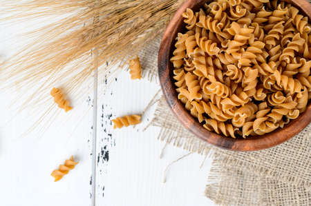 Bowl of wholegrain pasta spirals or fusilli, over light wooden background. Copy spaceの写真素材
