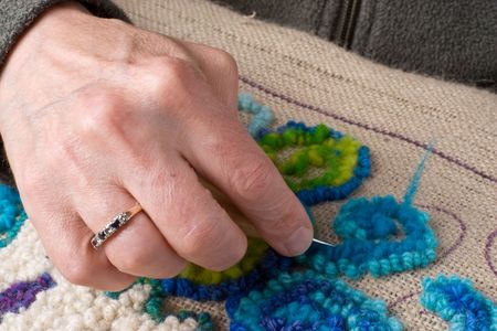 Detail showing a hand hooking a rug, a traditional maritime craft that recyles old fabrics into vibrant mats using burlap. の写真素材