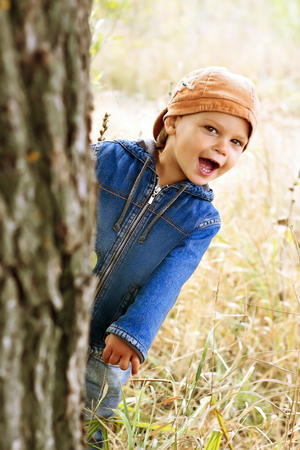 Kid in denim jacket peeping from behind a tree.の写真素材