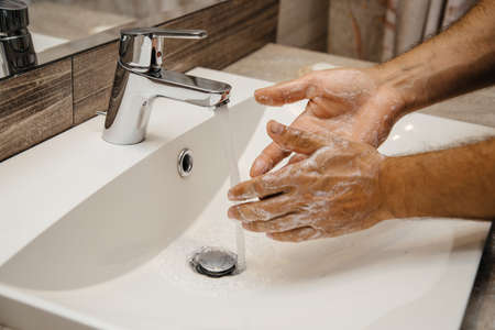 Human is washing hands with soap for corona virus prevention. Water flows from the water mixer and a man lathers his hands for stopping the spread of infection coronavirusの写真素材