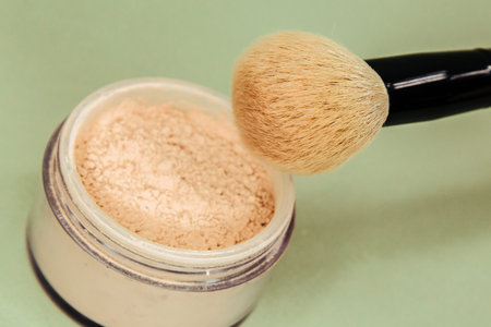 Makeup brush and powder on a green background. Close-up