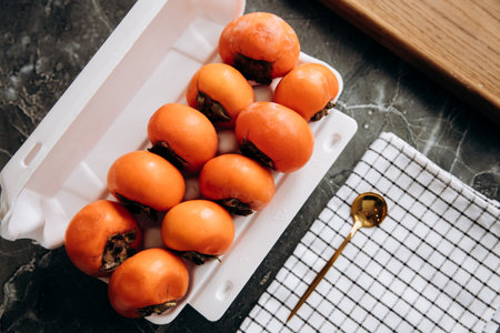 Ripe persimmons in a white container on a served marble table, top viewの写真素材