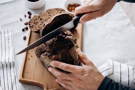 Female hands cut rye bread on a cutting board with a knife.の写真素材