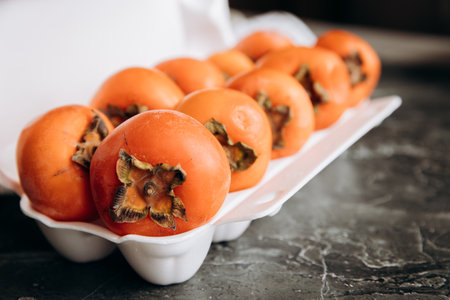 Fresh ripe persimmons in a white bowl on a dark backgroundの写真素材