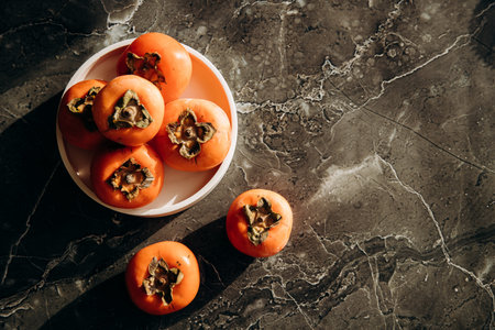 Ripe persimmon fruits in a bowl on a marble background