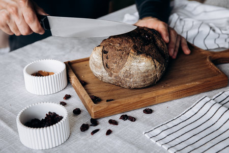 Male hands cut a loaf of bread with a knife on a cutting board.の写真素材
