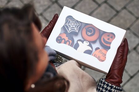 Young woman holding a colsed box full of different Halloween styled cupcakesの写真素材