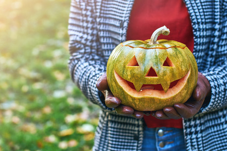 Woman hands in leather gloves holds a Halloween pumpkin outdoor in the autumn parkの写真素材