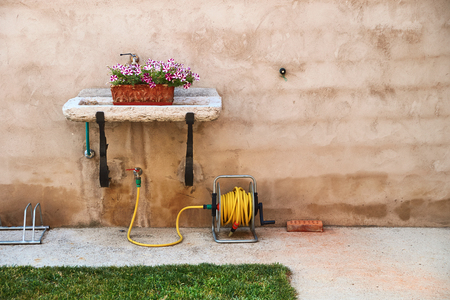 Decorative flower box in a garden sink and a yellow hoseの写真素材