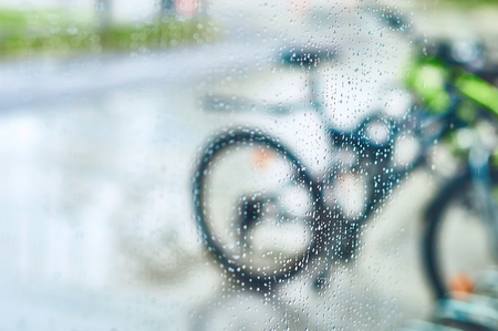 View of parked bicycles through the wet window glass with drops of waterの写真素材