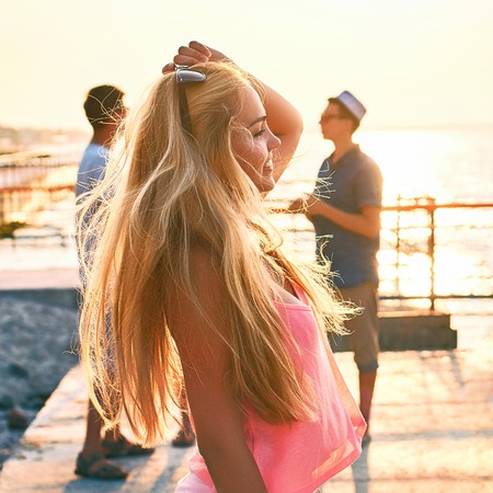 Young beautiful blonde girl in pink top having fun at the evening seaside with her friends on backgroundの写真素材
