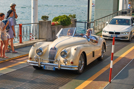 Happy man drives out his vintage beige Jaguar XK120, a sports car manufactured by Jaguar circa 1950,...