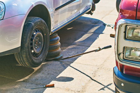 Changing wheels or tires on an grey automobile at an outdoor car service with old jackの写真素材