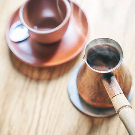Hot coffee with steam in oriental Turkish style served in cezve, a small long-handled pot with a pouring lip and cup on a wooden tableの写真素材