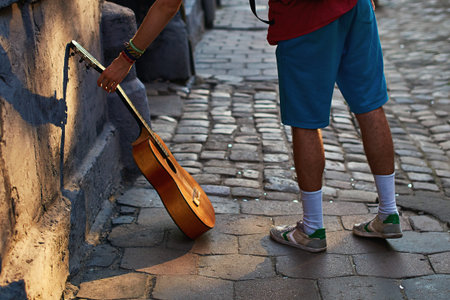 Young hippie musician reaches for his acoustic guitar on the old town street with cobblestones