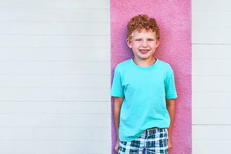 Cute red curly boy smiling and standing on wall backgroundの写真素材