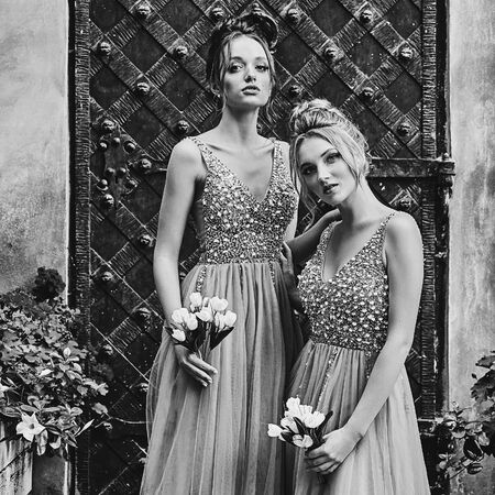 Beautiful bridesmaids in gorgeous elegant stylish floor length v neck chiffon gown dress decorated with sequins sparkles and rhinestones holding flowers bouquets. Wedding day in old beautiful European city. Black and white.の写真素材