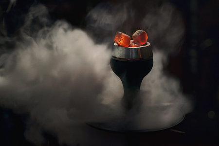 Trendy hookah bowl with red hot coals in clouds of beautiful white smoke on dark black background....