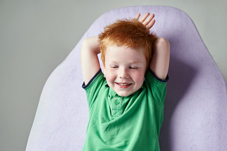 Cute red haired freckled little boy in green t-shirt waiting for doctor in medical officeの写真素材