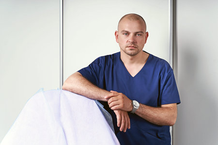 Experienced male massage therapist doctor or masseur in his medical office standing by a massage table wearing professional uniform.の写真素材