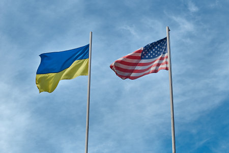 Flags of Ukraine and USA - United States of America waving in the wind at poles on cloudy sky backgroundの写真素材