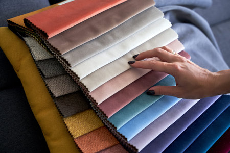 Choosing upholstery fabric color and texture from various colorful samples in a store. Female...