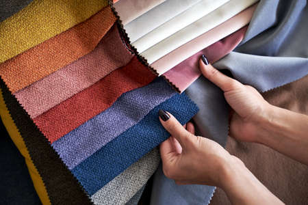 Choosing upholstery fabric color and texture from various colorful samples in a store. Female customer hands touching textile.の写真素材