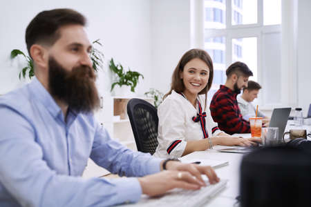 People communicating and working in modern IT office. Group of young and experienced programmers and software developers sitting at desks working on computers. Team at work.の写真素材