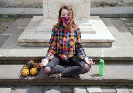 Young female zero waster wearing a plaid handmade face mask medidates outdoor in the old city streetの写真素材