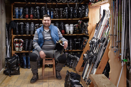 Portrait of cheerful SME ski rental service owner in an interior full of skis, boots, helmets, and other winter sport equipment for rent or saleの写真素材