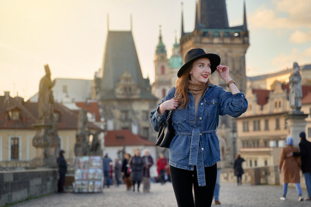 Female traveller tourist on the Charles Bridge in Prague, Czezh Repubic. Stylish beautiful young woman earing black hat. Elegant retro lady fine art portrait.の写真素材