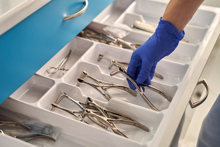 Doctors hands wearing a disposable medical gloves holding a stainless steel nasal speculum for ENT examination over other surgery instrumentsの写真素材
