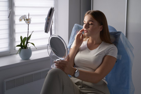 Young beautiful woman customer with mirror getting ready for beauty procedures in a medical salonの写真素材
