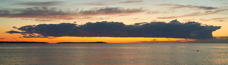 Long big dark cloud over the sea at sunsetの写真素材