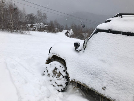 Snow covered off-road vehicle SUV car parked outdoor on a winter ski slopeの写真素材