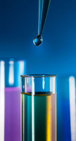 Laboratory pipette with a drop of substance over test tubes on blue backgroundの写真素材