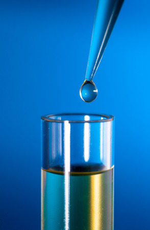 Laboratory pipette with a drop of substance over test tubes on blue backgroundの写真素材