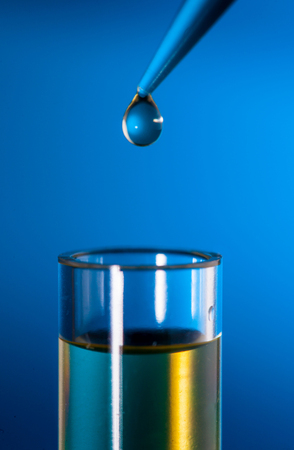 Laboratory pipette with a drop of substance over test tubes on blue backgroundの写真素材