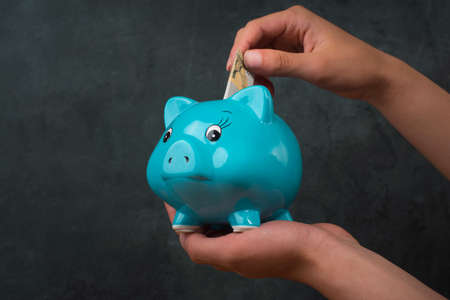 Putting money into a blue piggy bank, empty copy space for text, textured background, saving moneyの写真素材
