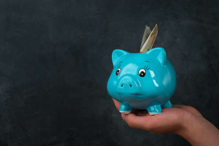Putting money into a blue piggy bank, empty copy space for text, textured background, saving moneyの写真素材