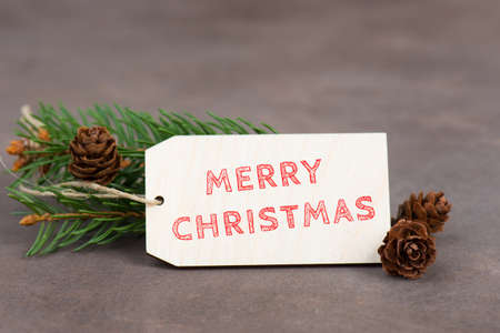 Merry christmas is standing on a sign, branch of fir and cones, textured brown backgroundの写真素材