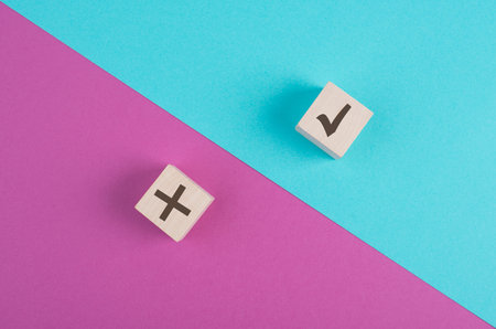 Wooden cubes with check mark and cross on a pink and blue colored vibrant background, minimalismの写真素材