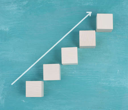 White arrow going up on wooden cubes, blue backgroundの写真素材
