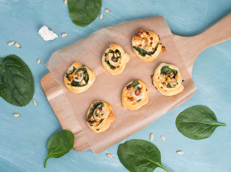 Puff pastry with spinach and feta cheese, rolled up to spirals, fresh from the oven, blue backgroundの写真素材